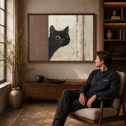 Walnut framed peeking black cat canvas art displayed above a seated man in a wood furnished room.