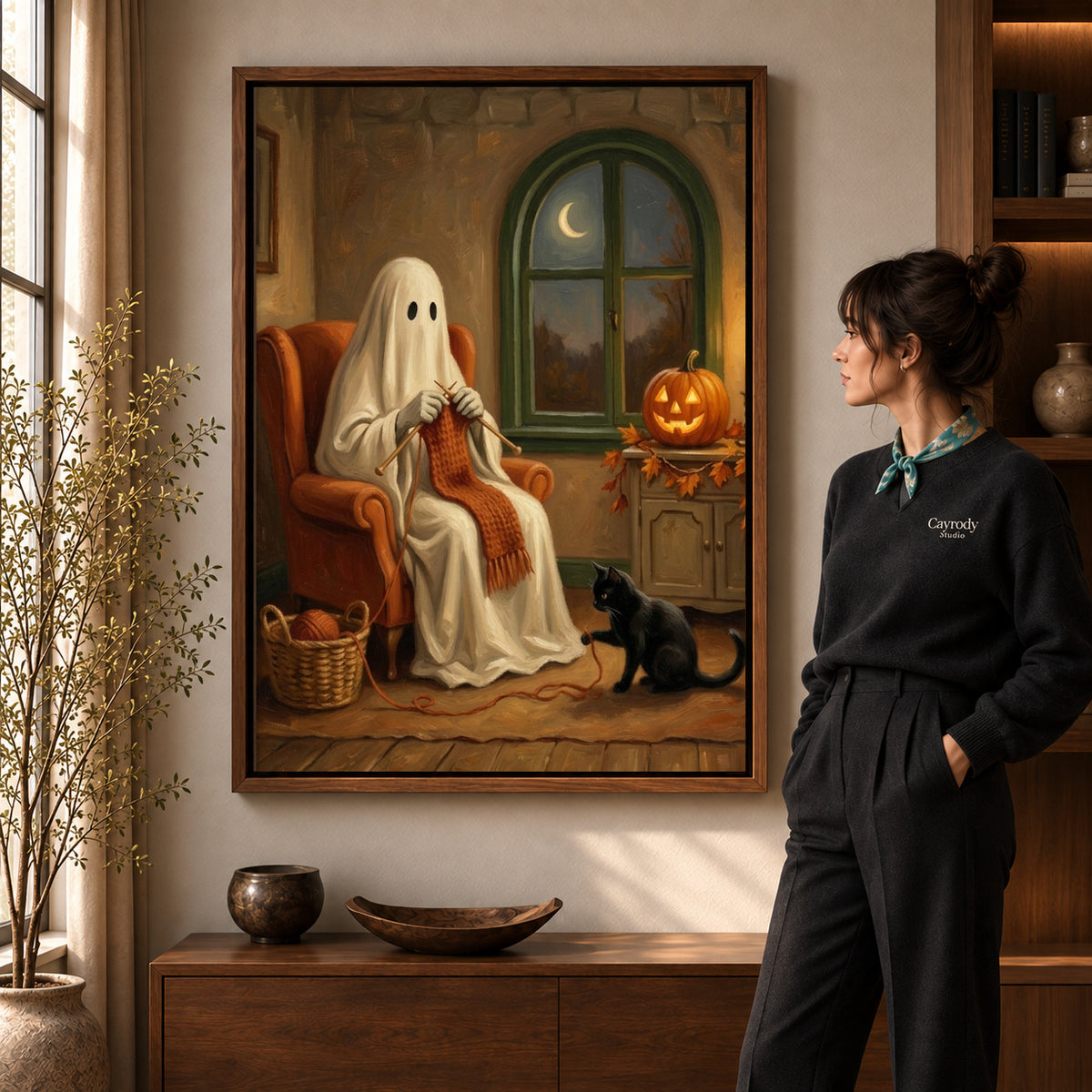 Cozy knitting ghost canvas art in a walnut frame beside a standing woman in a warm living room.
