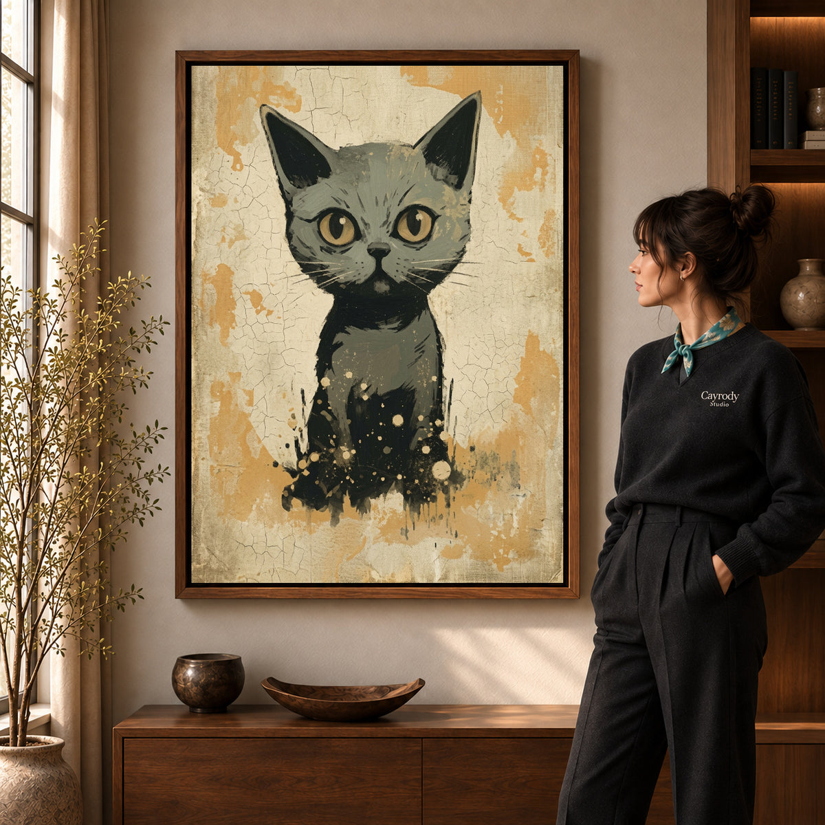 Golden eyed kitten canvas art in a walnut frame beside a standing woman in a warm living room.