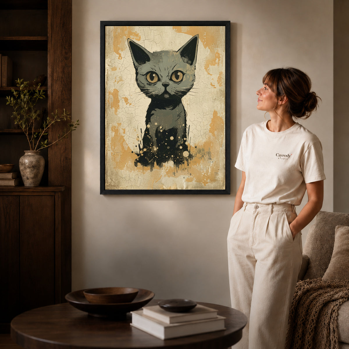 Black framed golden eyed kitten canvas art displayed beside a woman in a warm neutral living room.