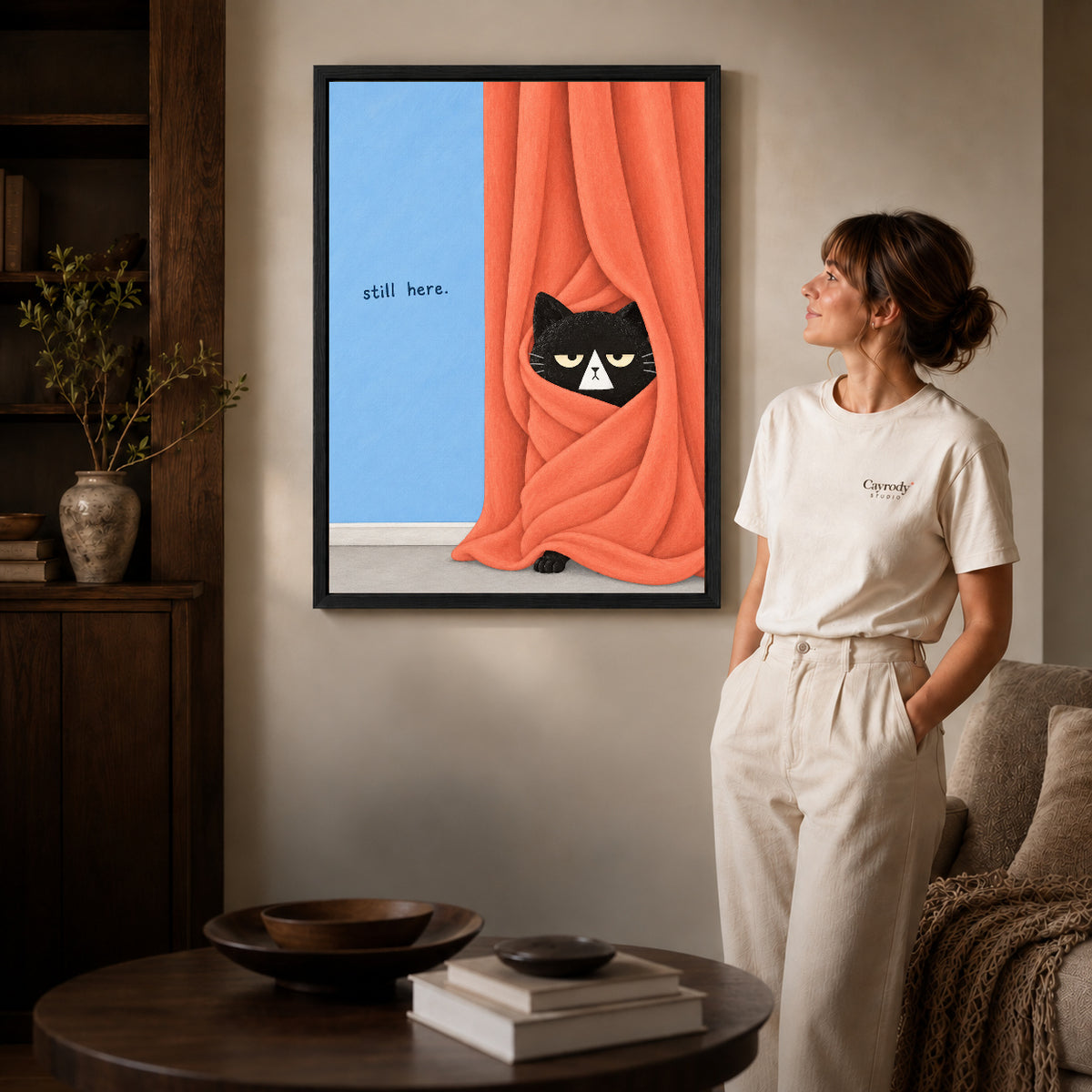 Black framed curtain black cat canvas art displayed beside a woman in a warm neutral living room.