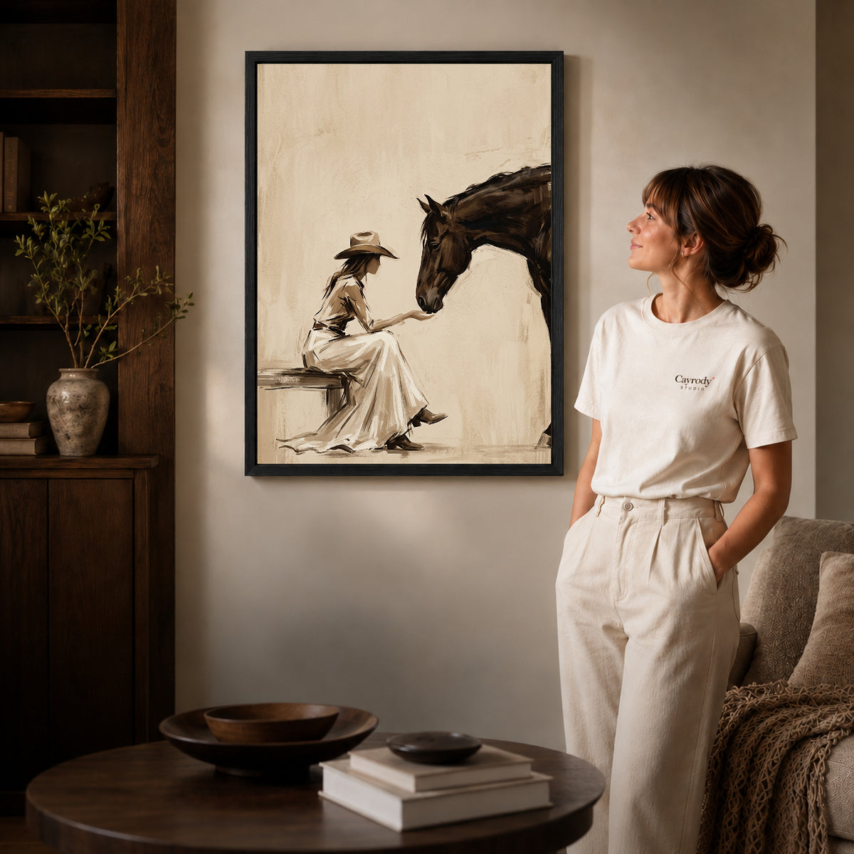 Black framed woman and horse canvas art displayed beside a woman in a warm neutral living room.