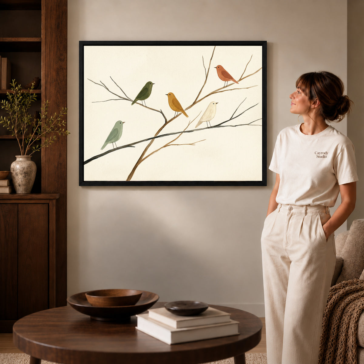 Black framed birds on branches canvas art displayed beside a woman in a warm neutral living room.