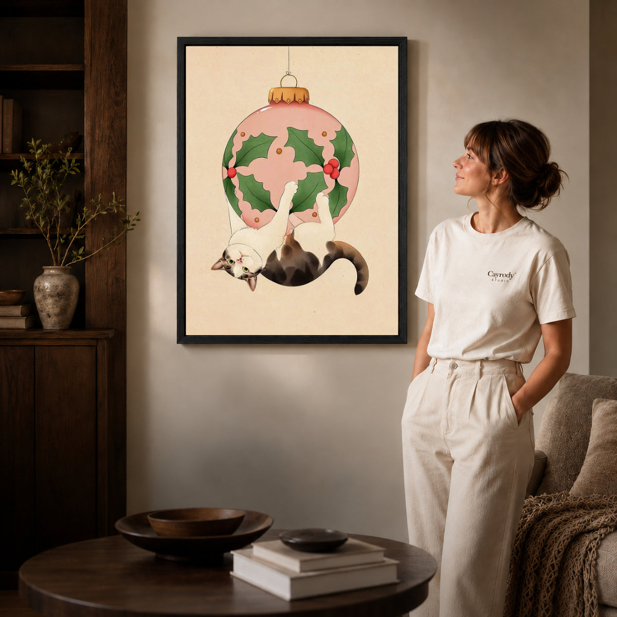 Black framed hanging holiday cat canvas art displayed beside a woman in a warm neutral living room.