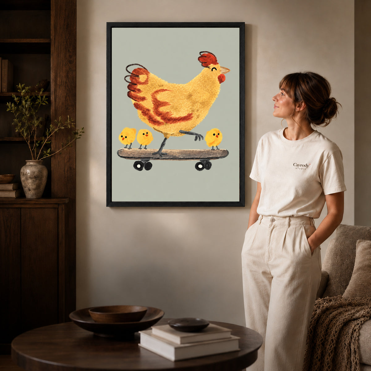 Black framed skateboard chicken canvas art displayed beside a woman in a warm neutral living room.