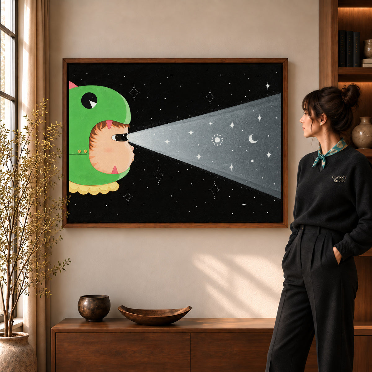 Dinosaur Hood Cat artwork in a walnut frame beside a standing woman in a warm room.