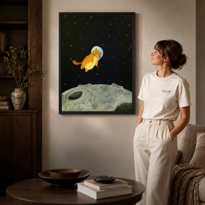 Black framed space kitten canvas art displayed beside a woman in a warm neutral living room.
