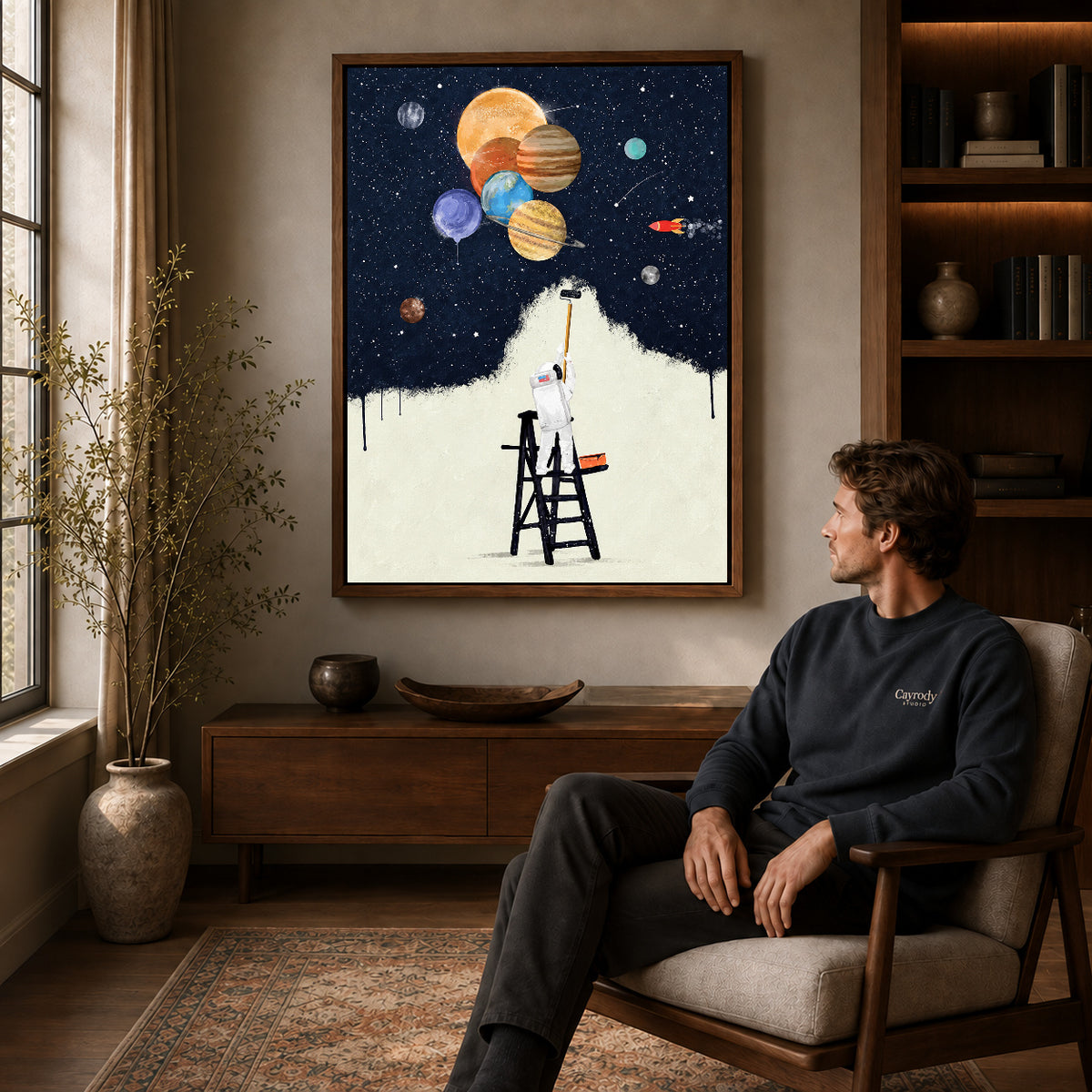 Walnut framed astronaut painter canvas art displayed above a seated man in a wood furnished living room.