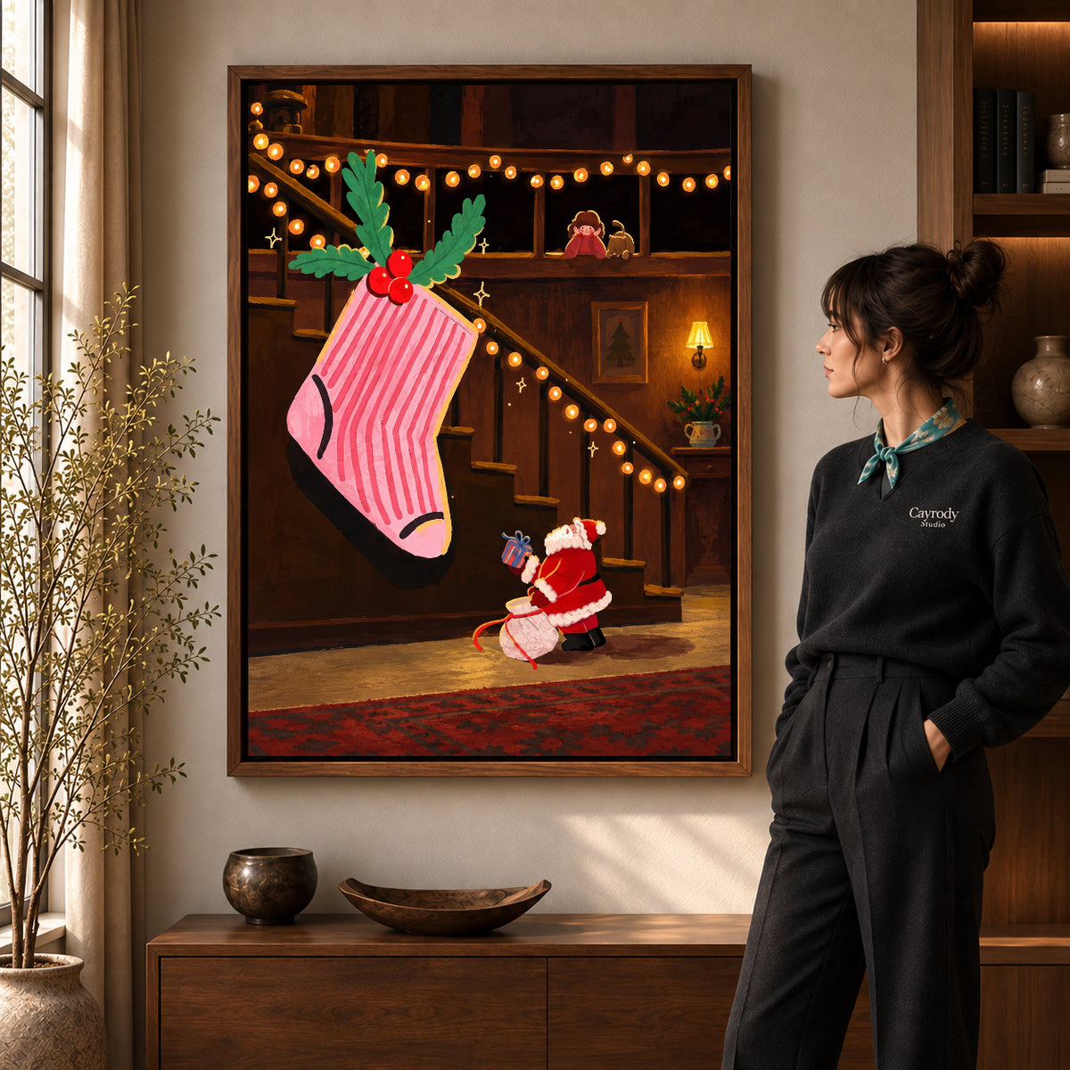 Giant Christmas Stocking artwork in a walnut frame beside a standing woman in a warm room.