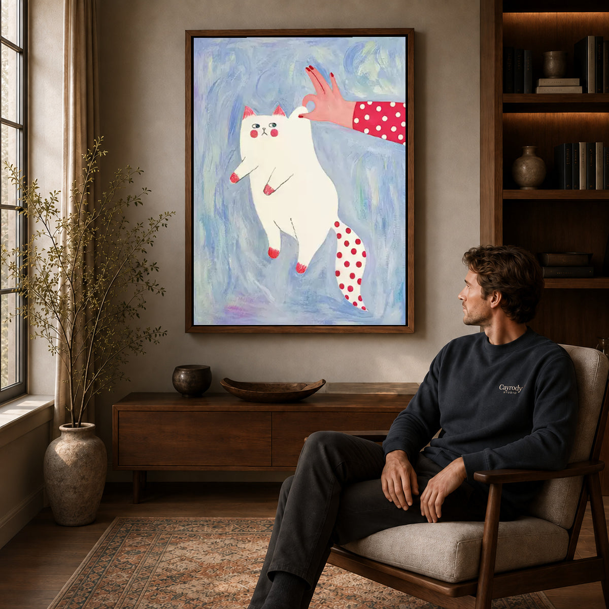 Walnut framed playful white cat canvas art displayed above a seated man in a wood furnished living room.