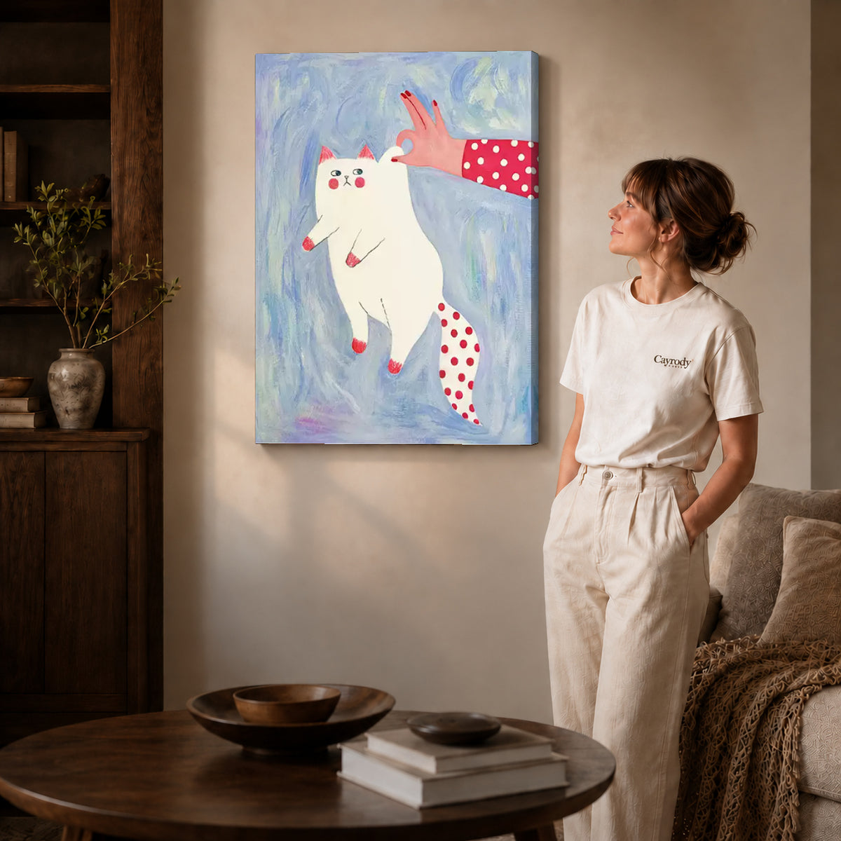 Gallery wrapped playful white cat canvas art with naturally shaded canvas edges beside a woman wearing cream clothing.