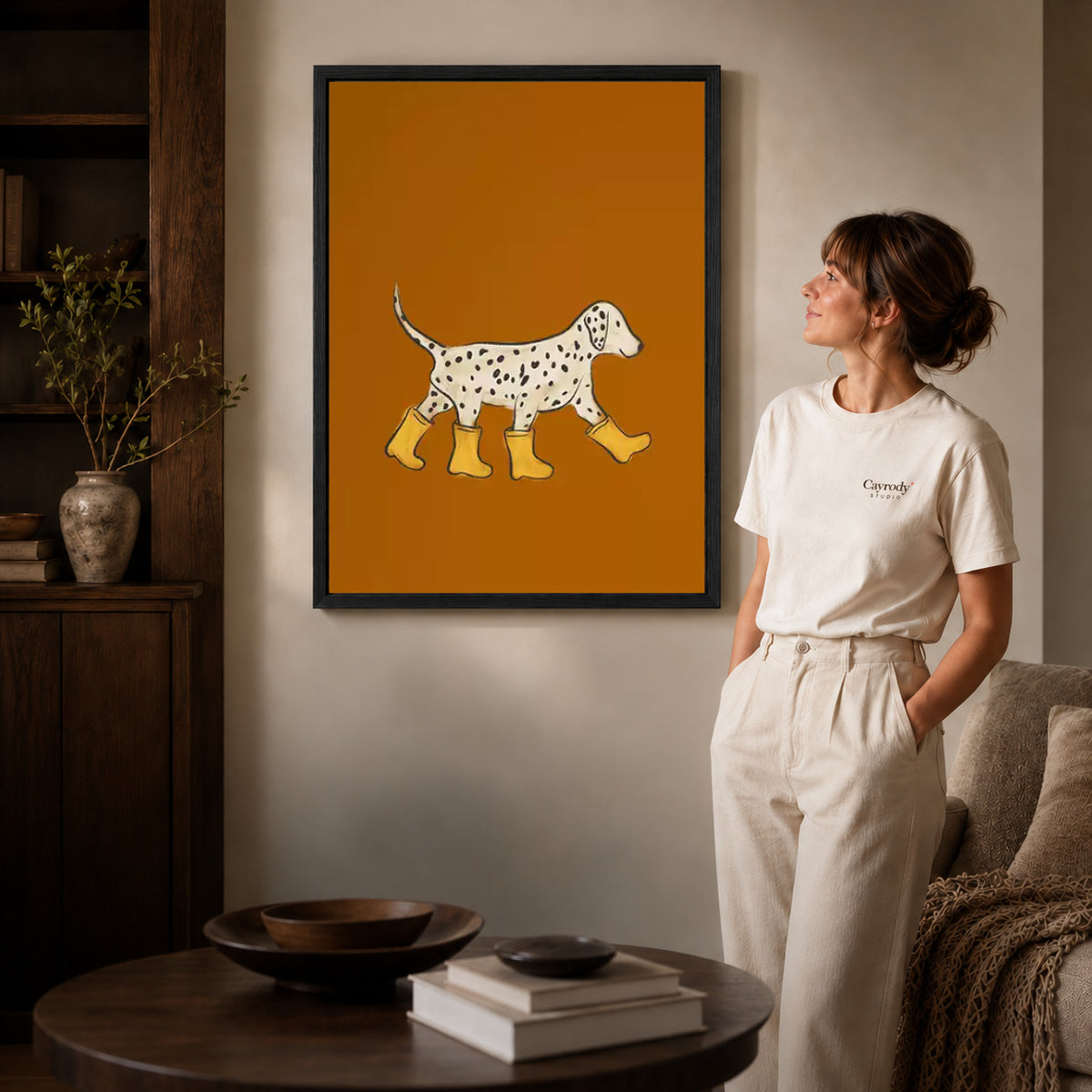 Black framed rain boot dalmatian canvas art displayed beside a woman in a warm neutral living room.