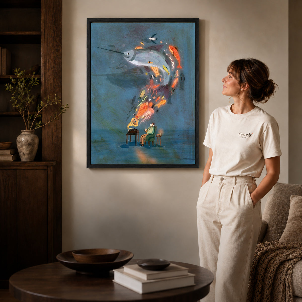 Black framed ocean music dream canvas art displayed beside a woman in a warm neutral living room.