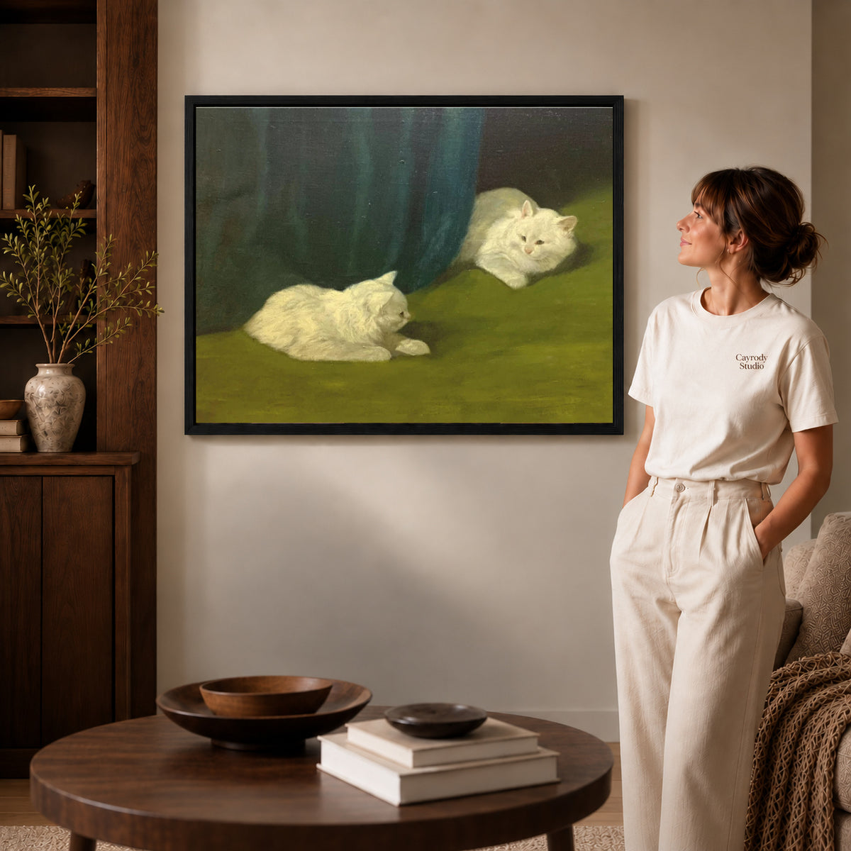 Black framed quiet white cats canvas art displayed beside a woman in a warm neutral living room.