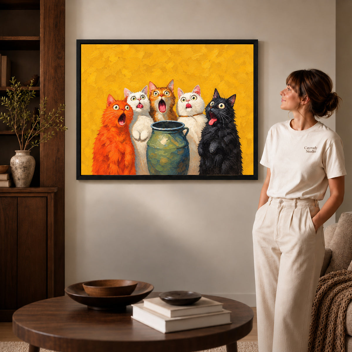Black framed surprised cat quintet artwork beside a woman in a warm neutral living room.