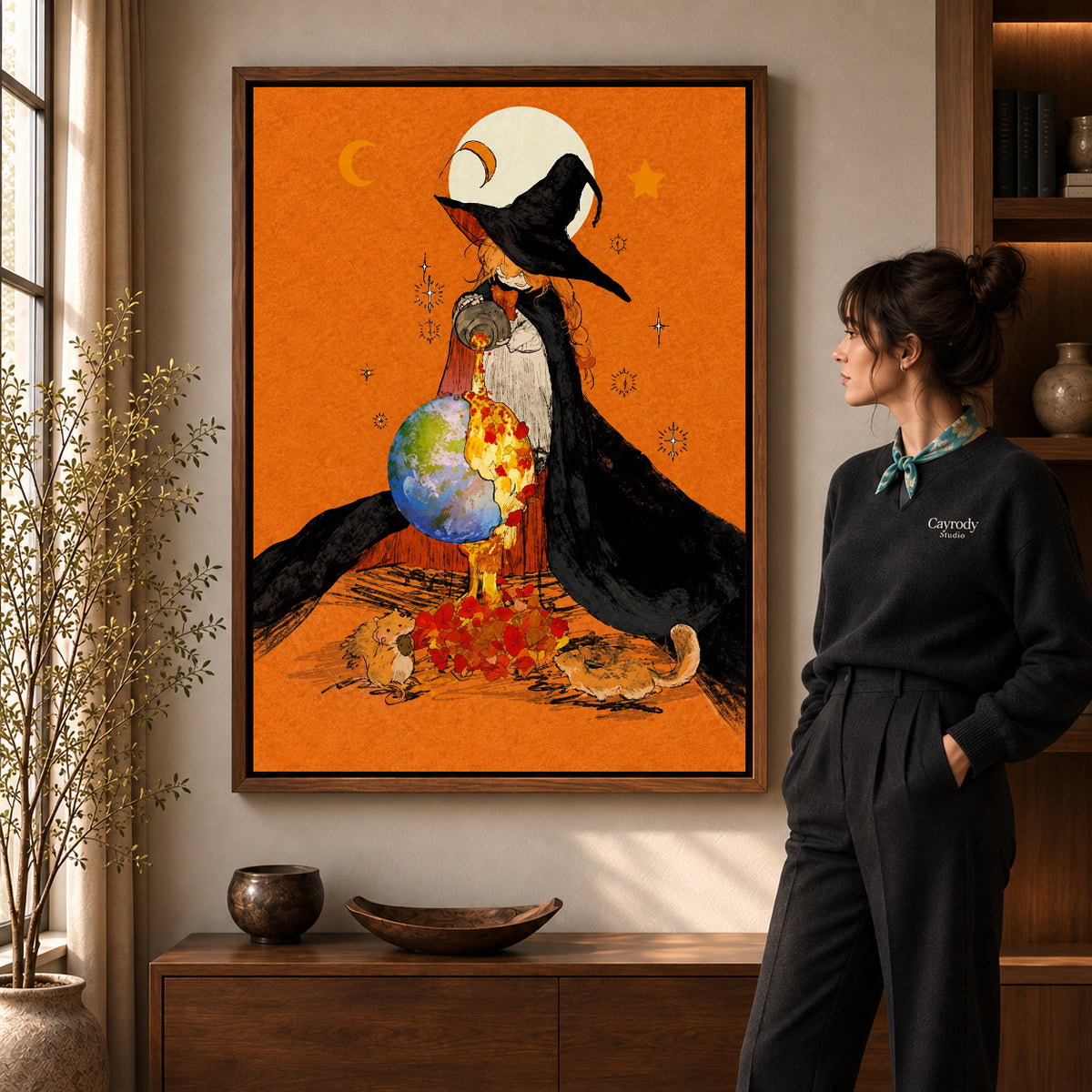 Autumn Globe Witch artwork in a walnut frame beside a standing woman in a warm room.