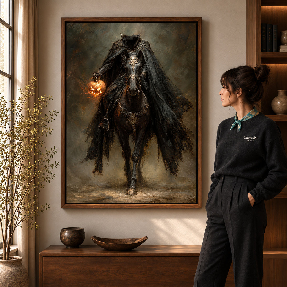 Headless Pumpkin Rider artwork in a walnut frame beside a standing woman in a warm room.