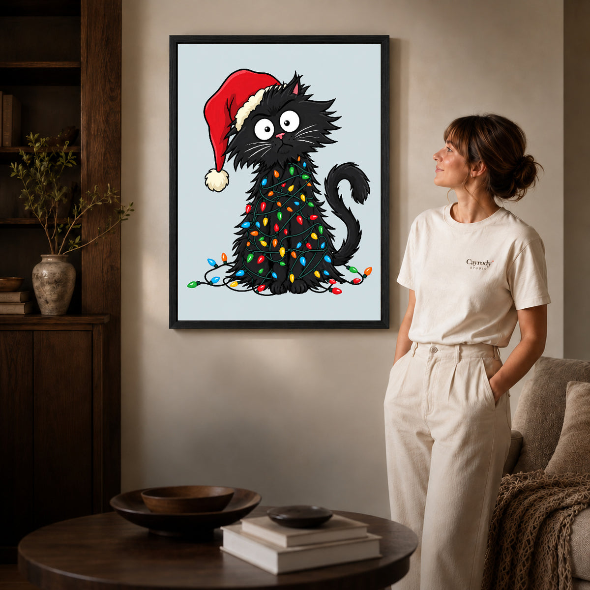 Black framed holiday lights cat canvas art displayed beside a woman in a warm neutral living room.