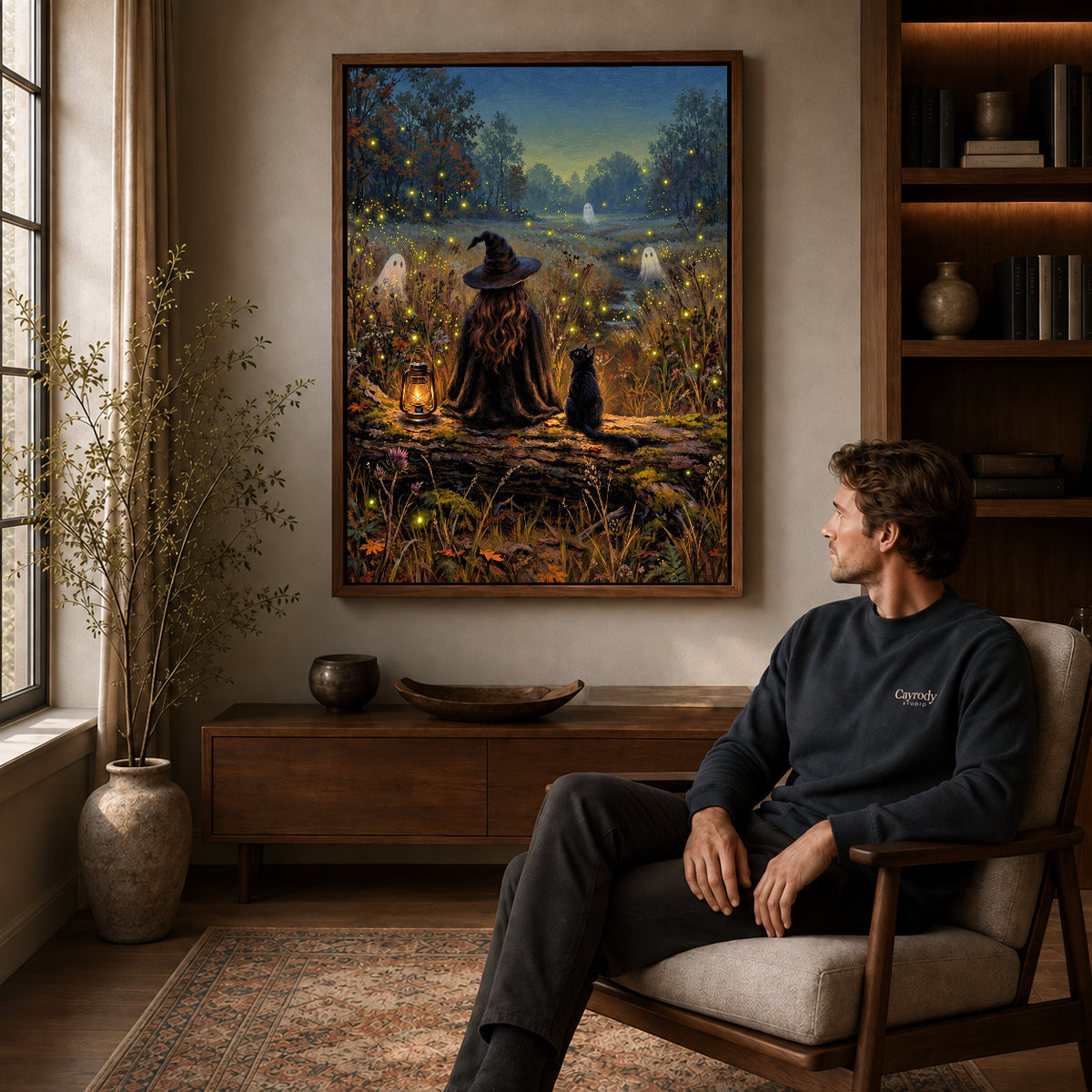 Walnut framed witch cat fireflies canvas art displayed above a seated man in a wood furnished room.
