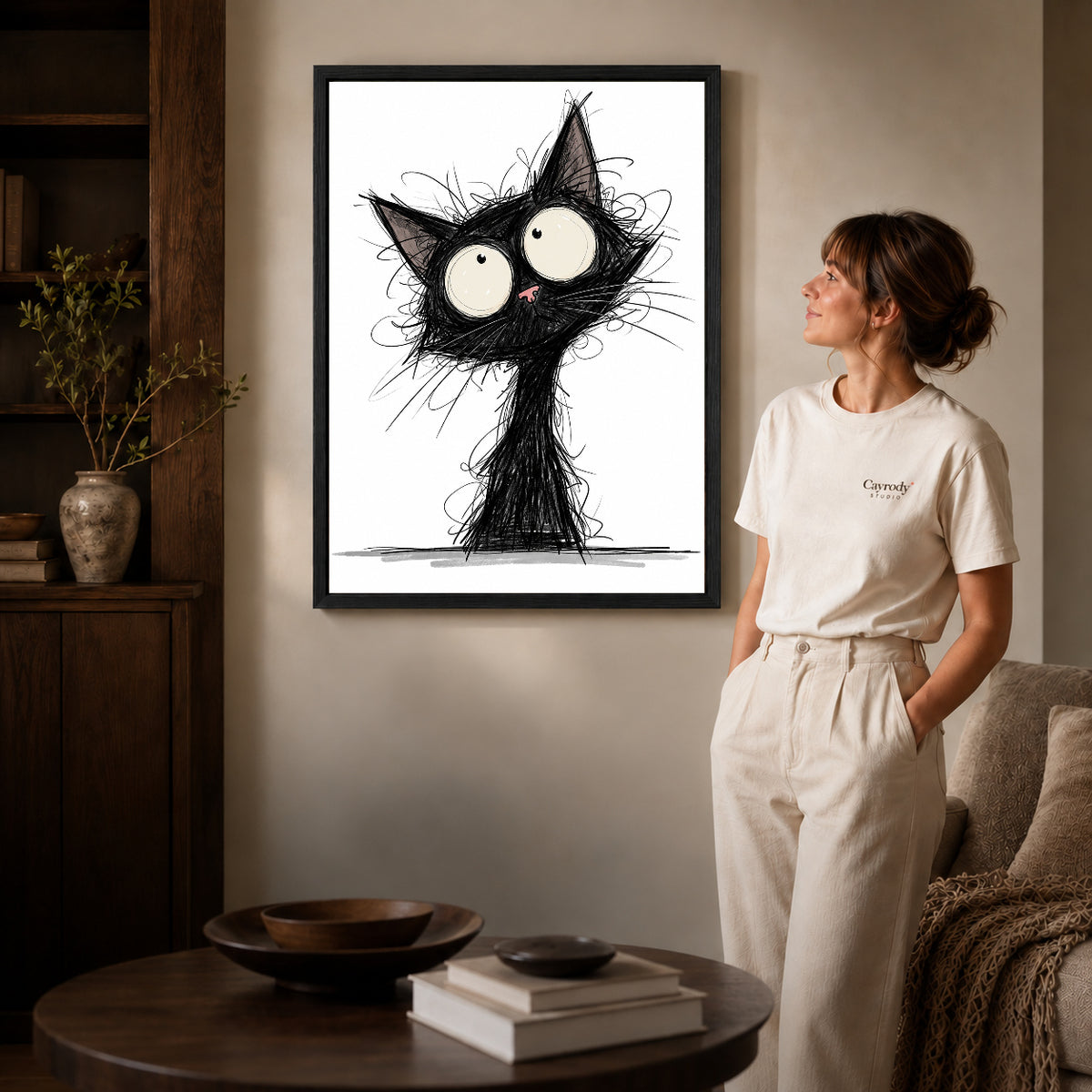 Black framed wide eyed sketch cat artwork beside a woman in a warm neutral living room.