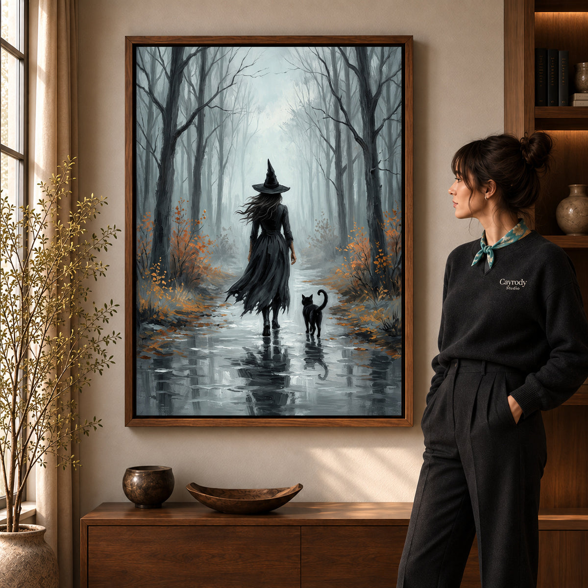 Misty Witch Walk artwork in a walnut frame beside a standing woman in a warm room.