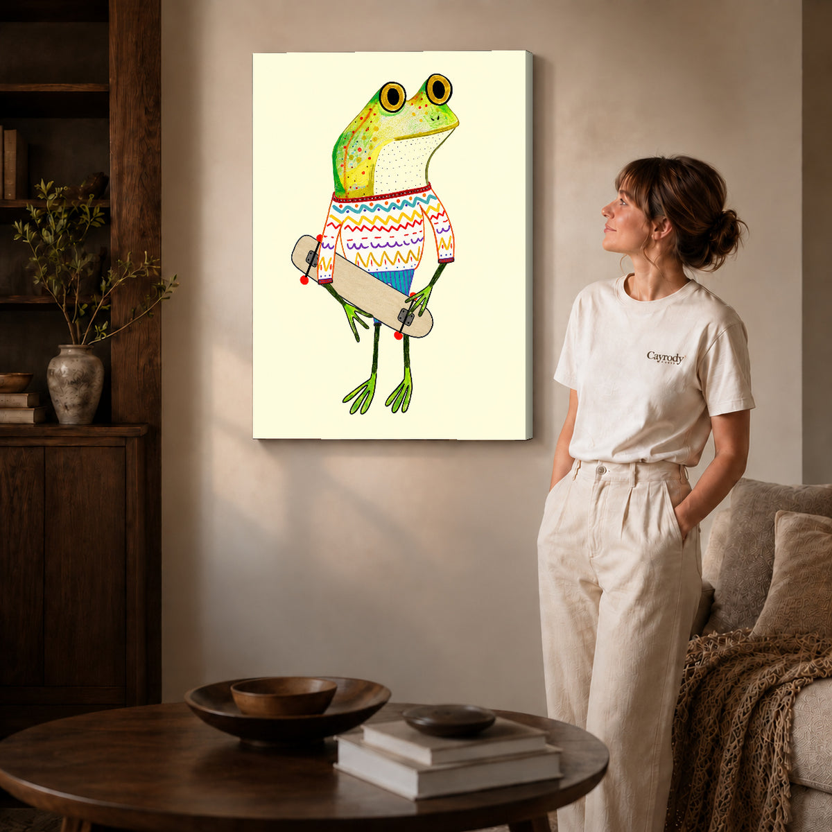 Gallery wrapped skateboard sweater frog artwork with shaded canvas edges beside a woman wearing cream clothing.