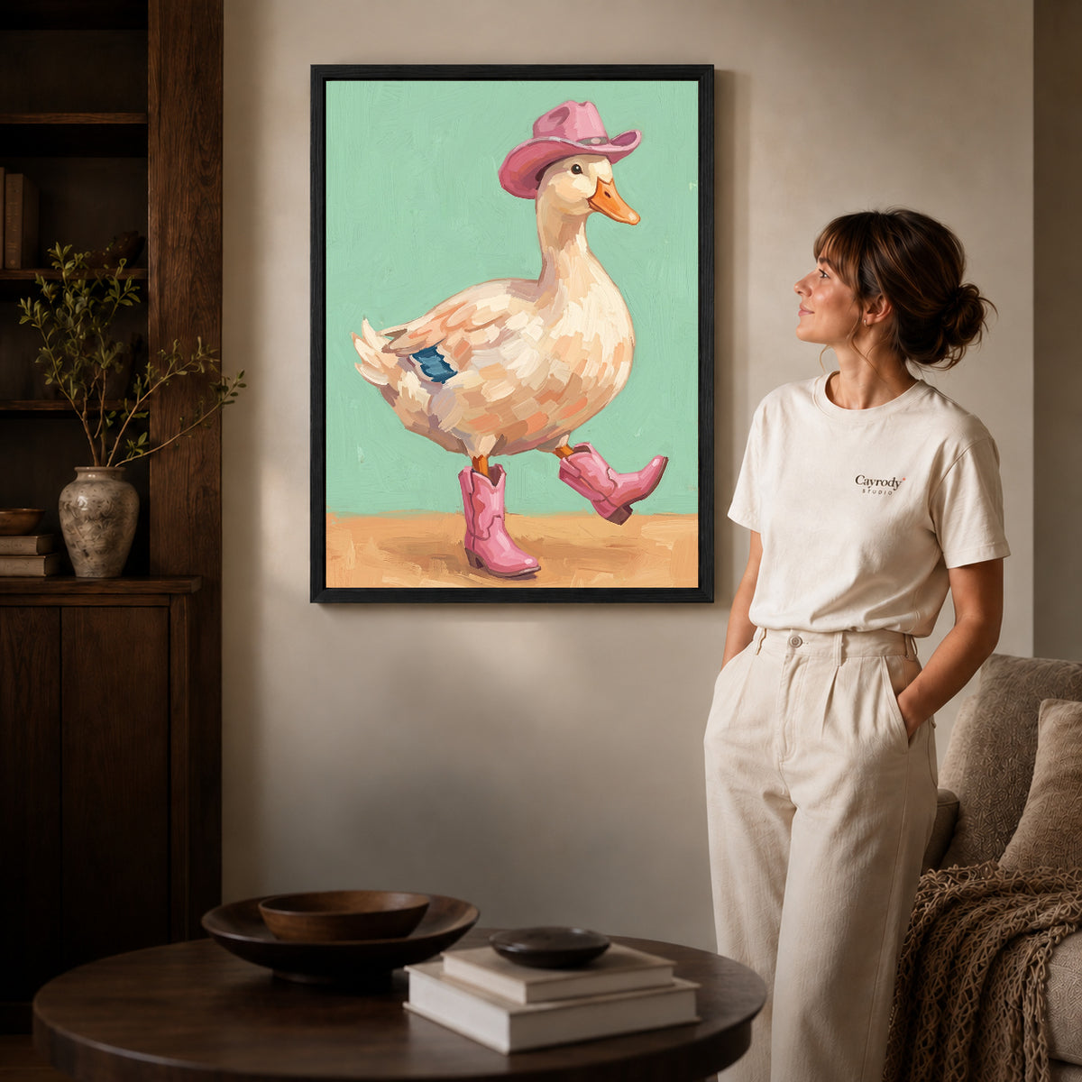 Black framed cowboy boots duck canvas art displayed beside a woman in a warm neutral living room.