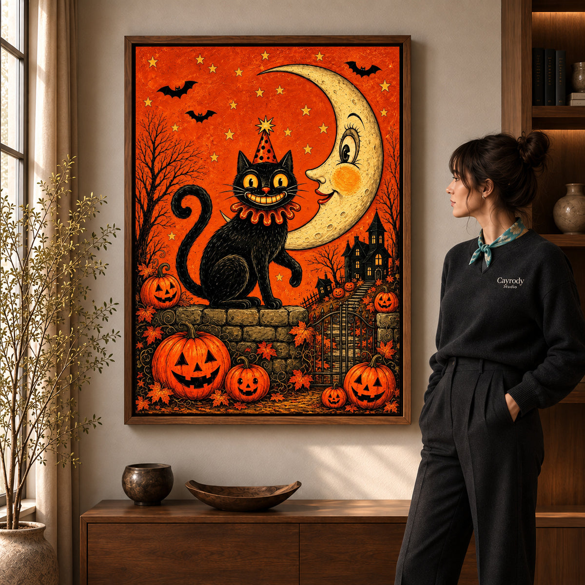 Crescent Halloween Cat artwork in a walnut frame beside a standing woman in a warm room.