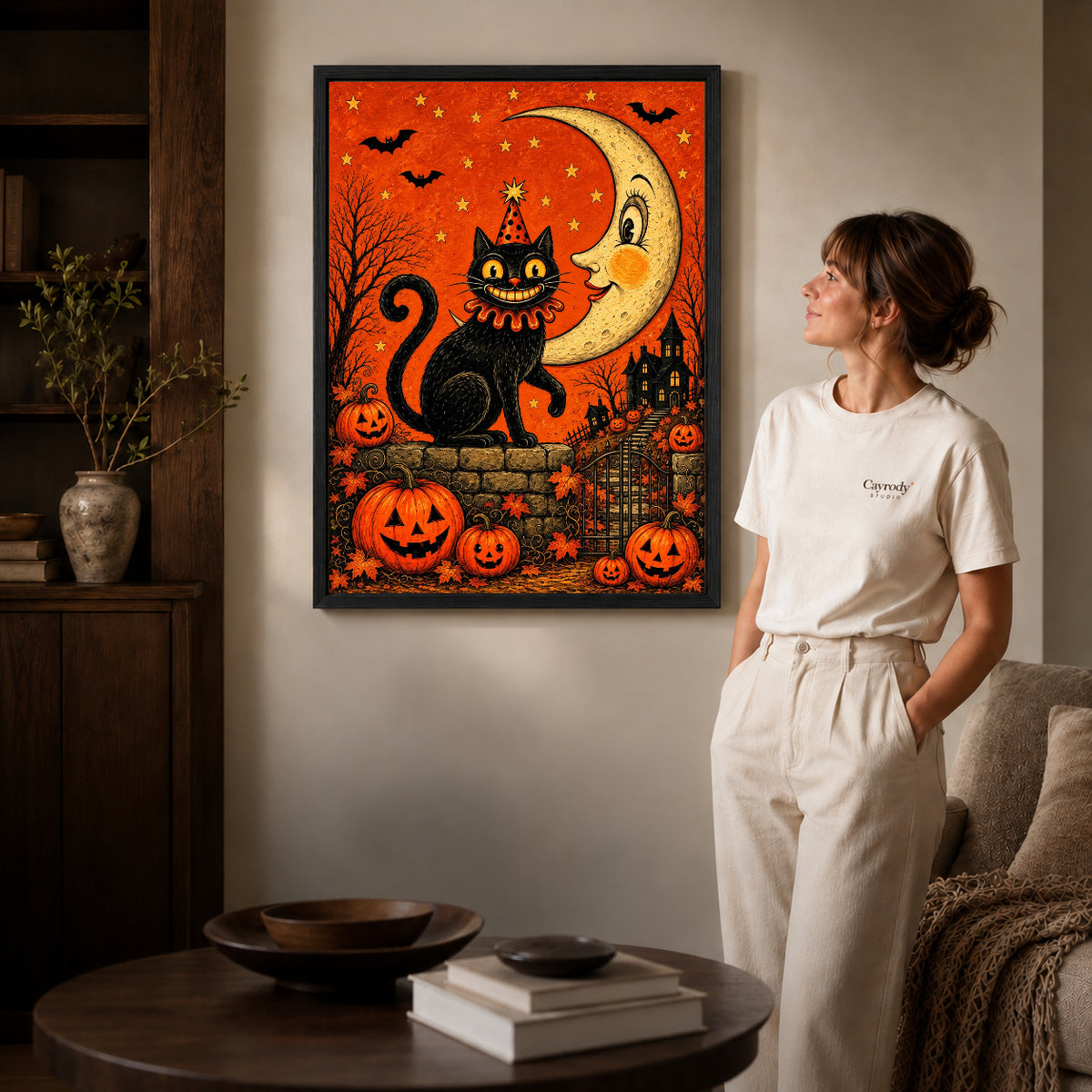 Black framed crescent halloween cat artwork beside a woman in a warm neutral living room.