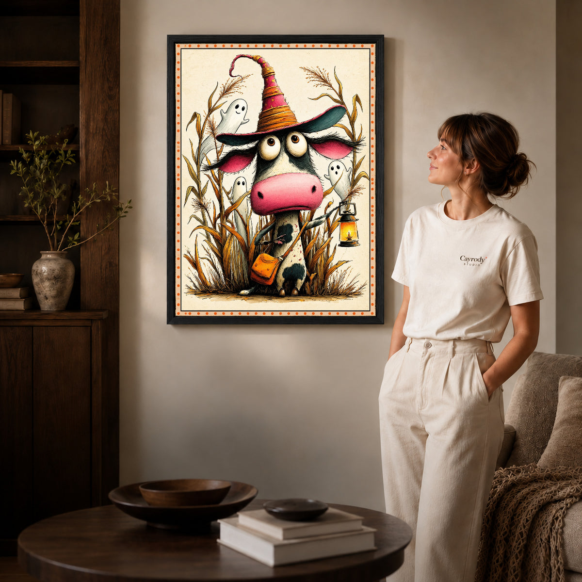 Black framed lantern witch cow artwork beside a woman in a warm neutral living room.