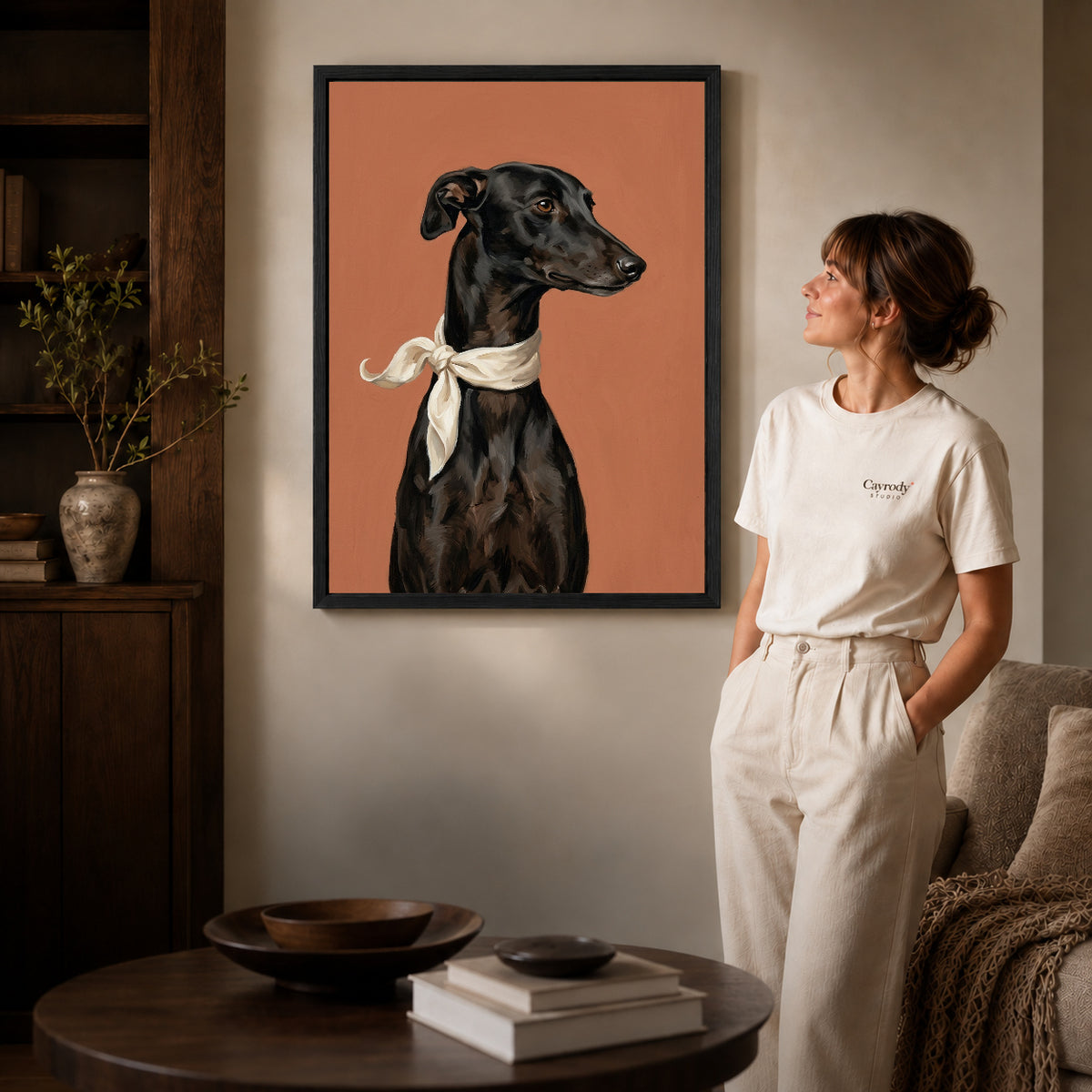 Black framed elegant greyhound portrait canvas art displayed beside a woman in a warm neutral living room.
