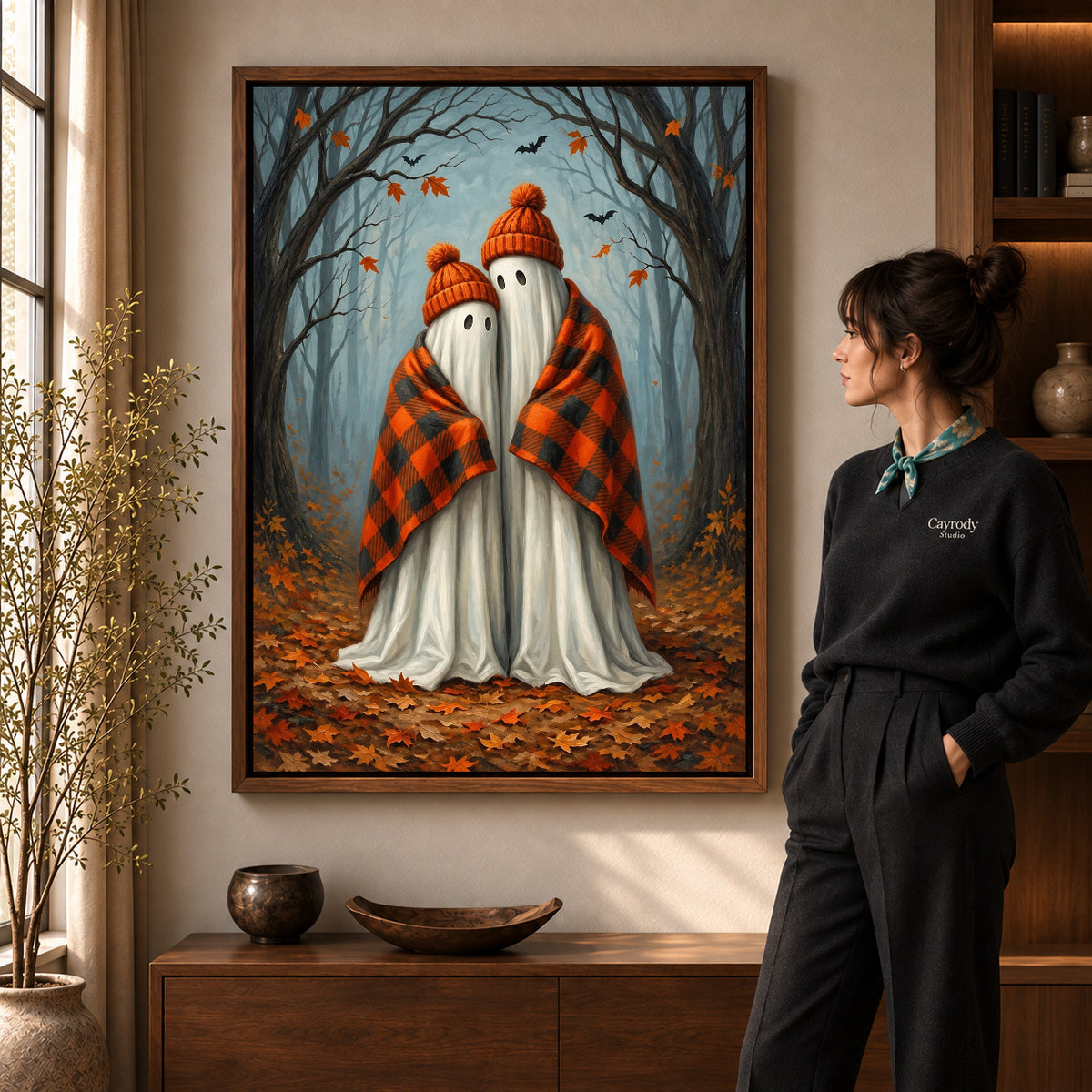 Cozy Autumn Ghosts artwork in a walnut frame beside a standing woman in a warm room.