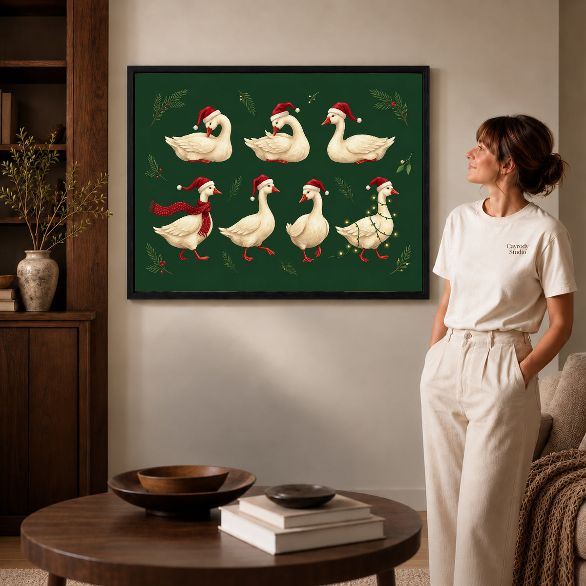 Black framed holiday goose flock canvas art displayed beside a woman in a warm neutral living room.