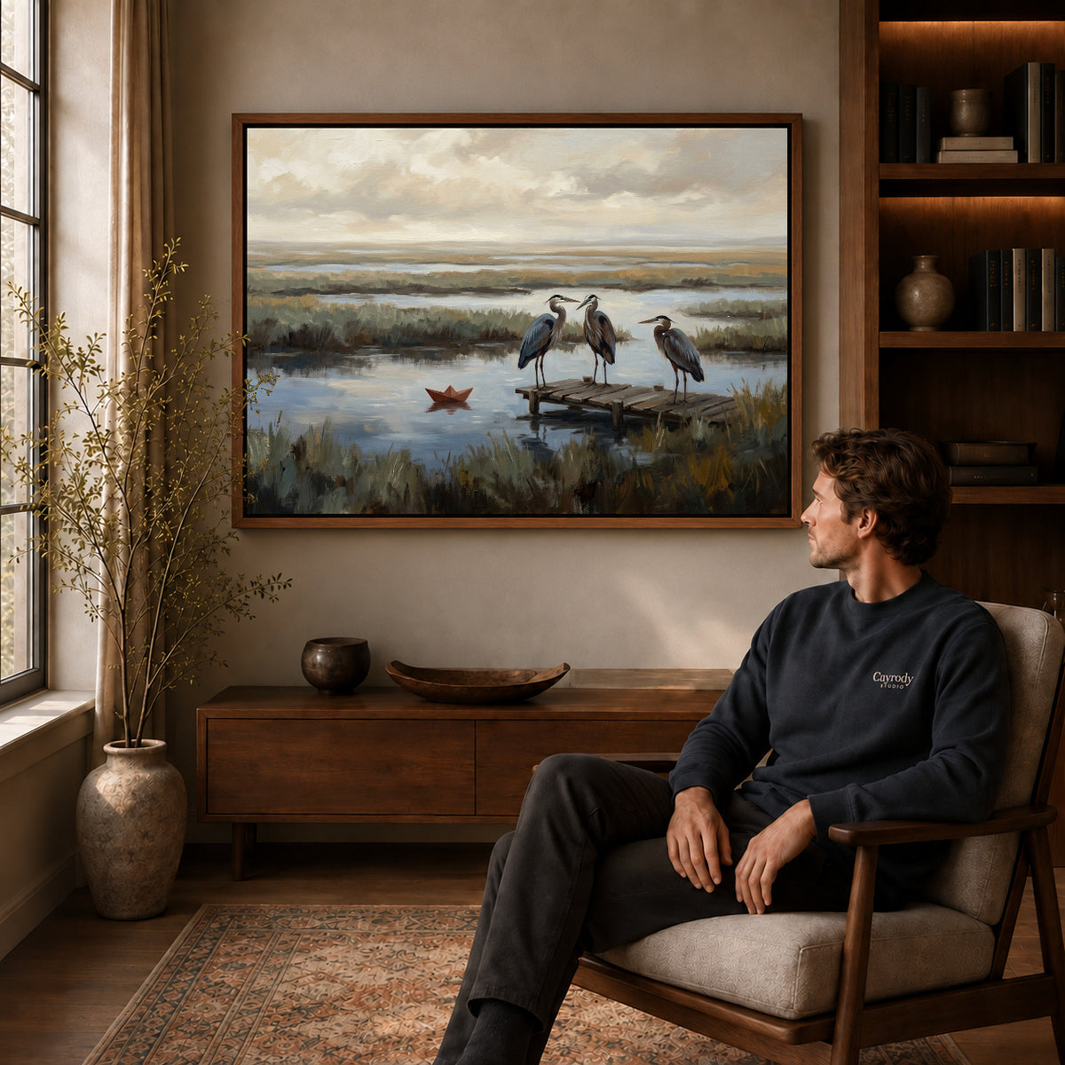 Walnut framed quiet marsh herons canvas art displayed above a seated man in a wood furnished room.
