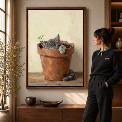 Sleeping kitten pot canvas art in a walnut frame beside a standing woman in a warm living room.