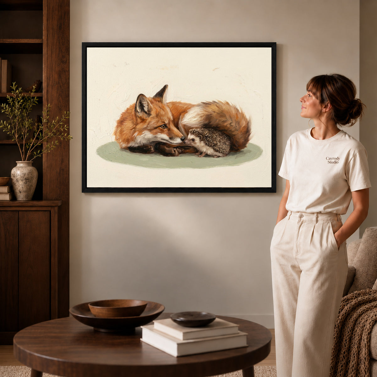 Black framed fox hedgehog friends canvas art displayed beside a woman in a warm neutral living room.