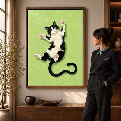 Stretching tuxedo cat canvas art in a walnut frame beside a standing woman in a warm living room.