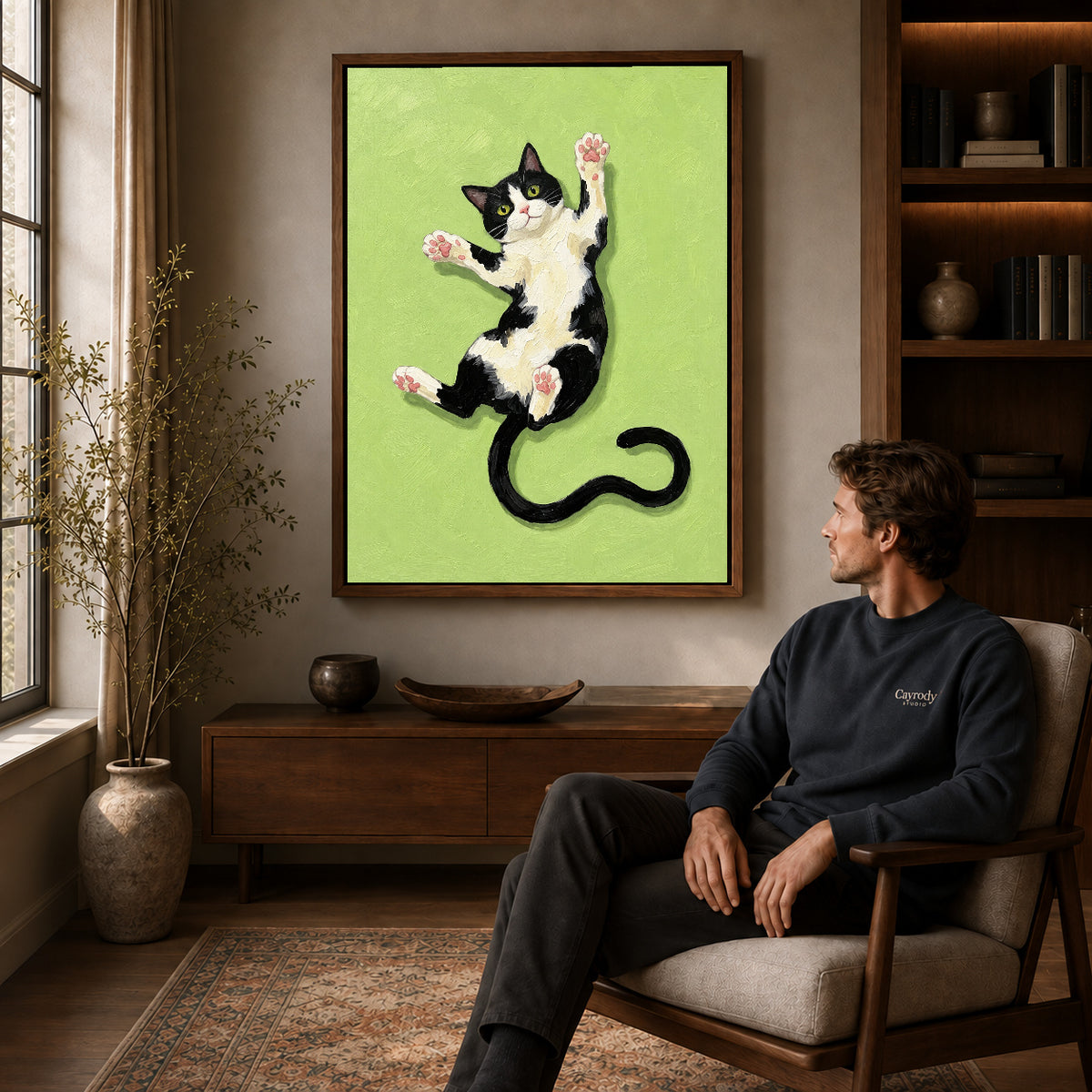 Walnut framed stretching tuxedo cat canvas art displayed above a seated man in a wood furnished room.