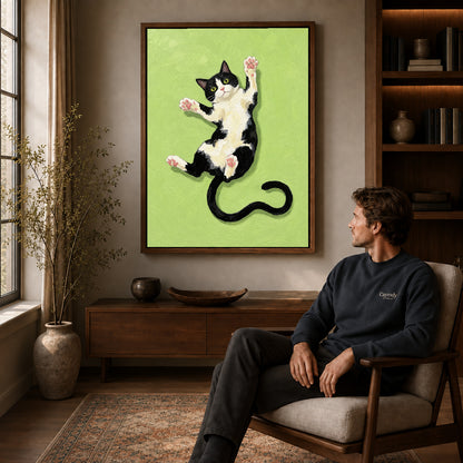 Walnut framed stretching tuxedo cat canvas art displayed above a seated man in a wood furnished room.