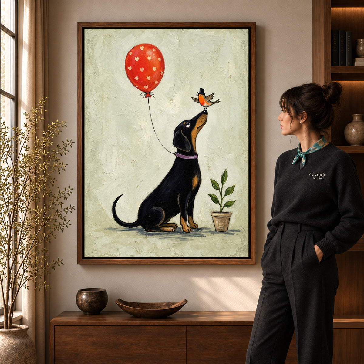 Balloon Bird Dachshund artwork in a walnut frame beside a standing woman in a warm room.