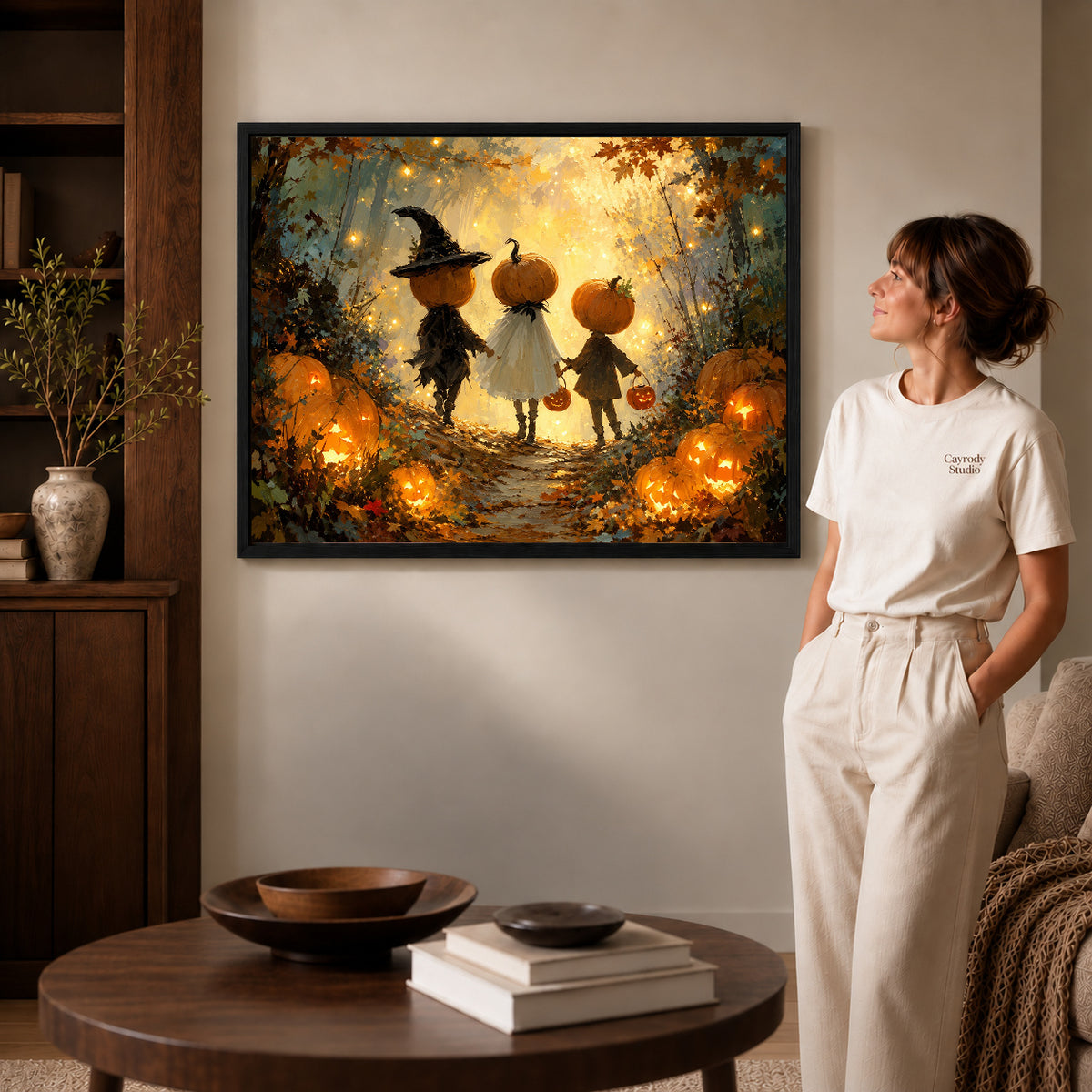 Black framed pumpkin forest trio artwork beside a woman in a warm neutral living room.