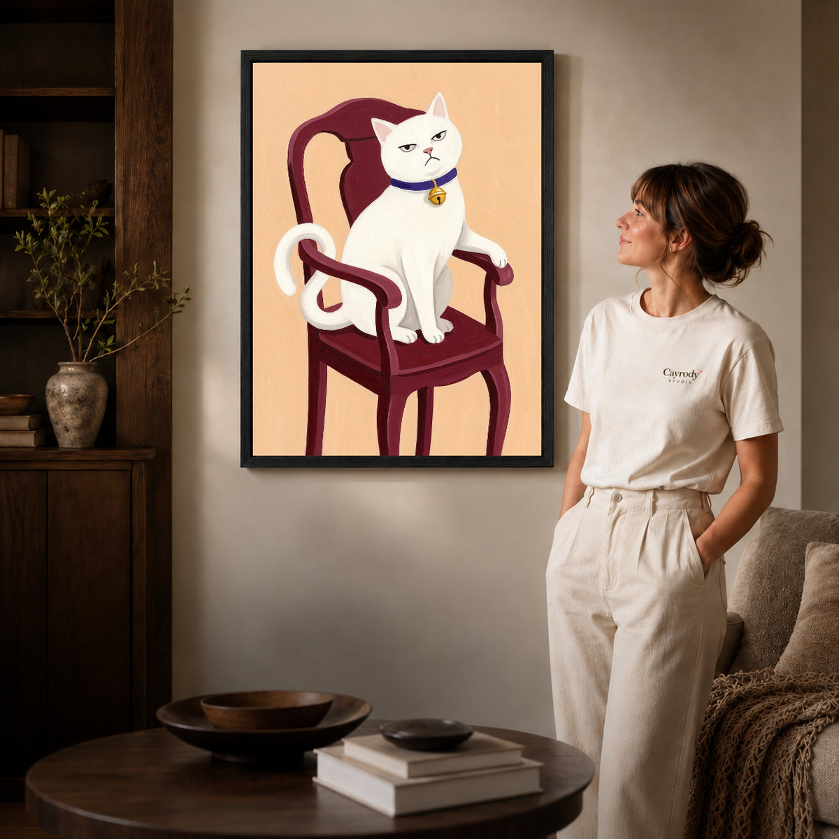 Black framed regal white cat artwork beside a woman in a warm neutral living room.