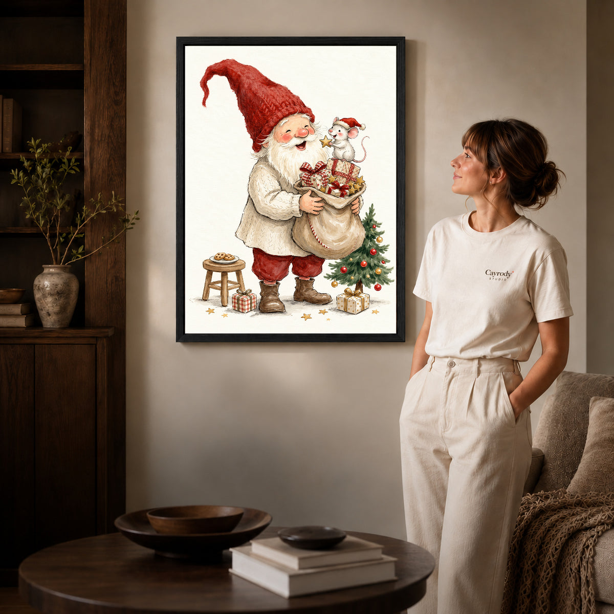 Black framed santa mouse surprise artwork beside a woman in a warm neutral living room.
