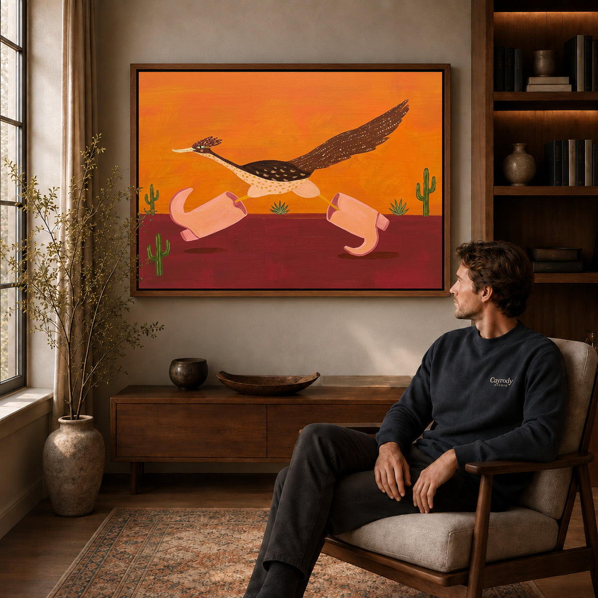 Walnut framed folk roadrunner pink boots canvas art displayed above a seated man in a wood furnished room.