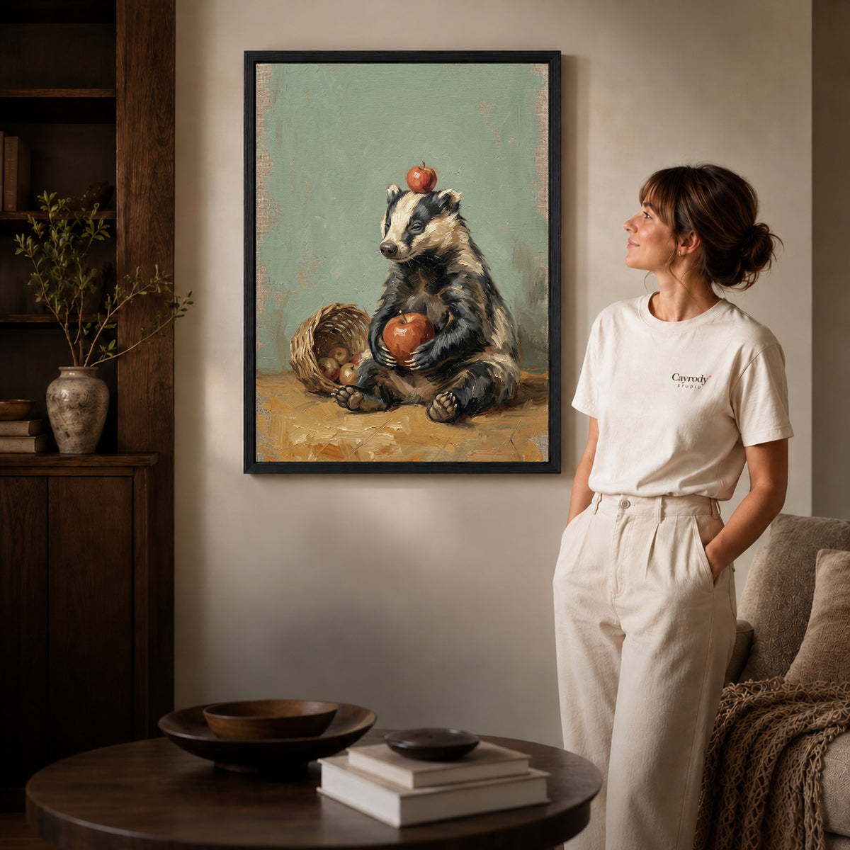 Black framed badger apple basket canvas art displayed beside a woman in a warm neutral living room.