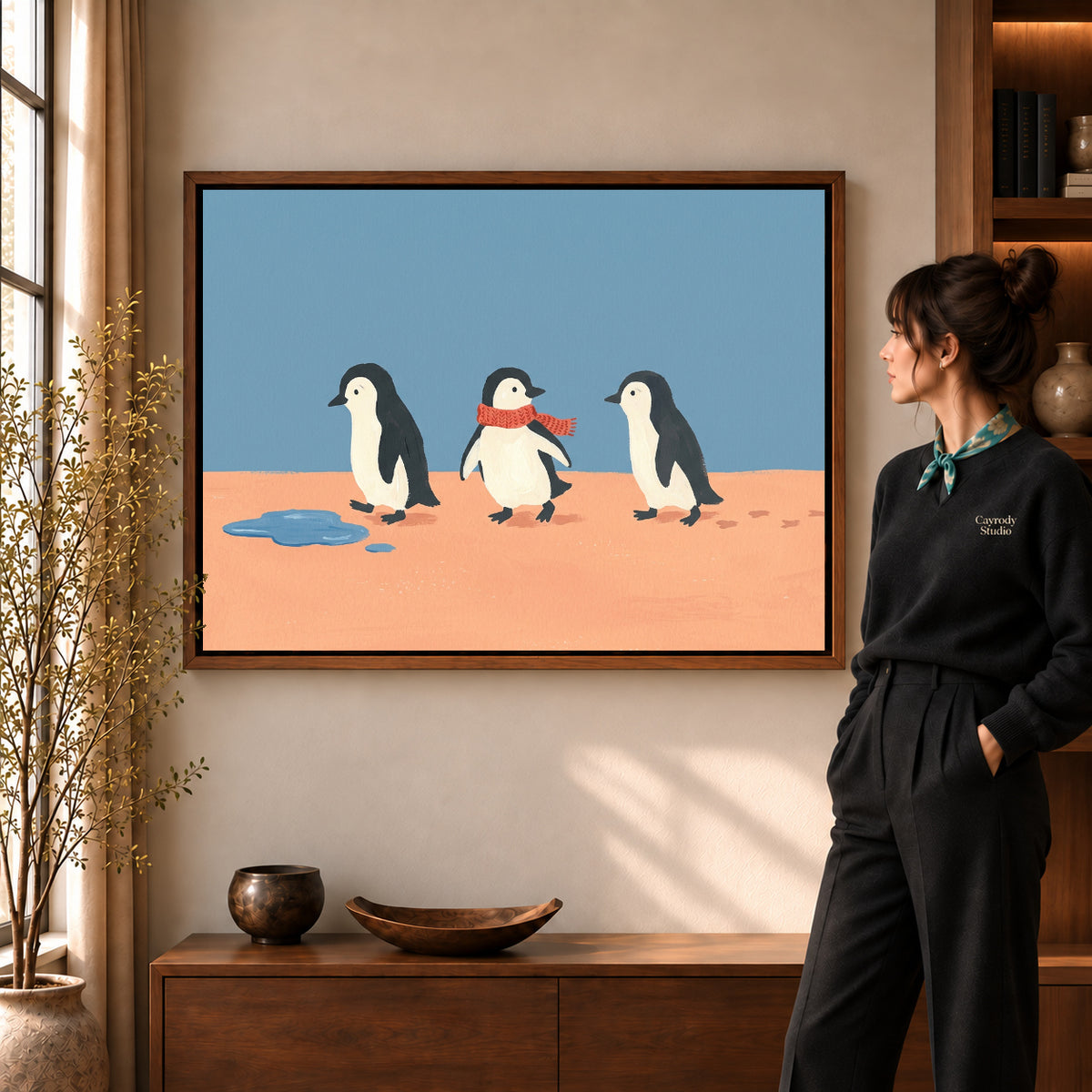 Three penguin friends canvas art in a walnut frame beside a standing woman in a warm living room.