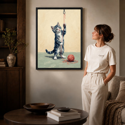 Black framed playful yarn kitten artwork beside a woman in a warm neutral living room.