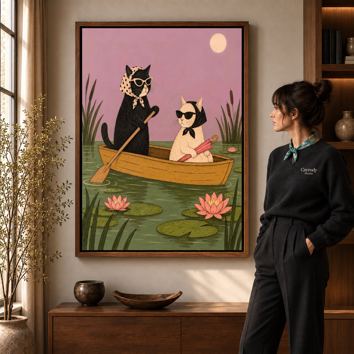 Boat Cat Friends artwork in a walnut frame beside a standing woman in a warm room.