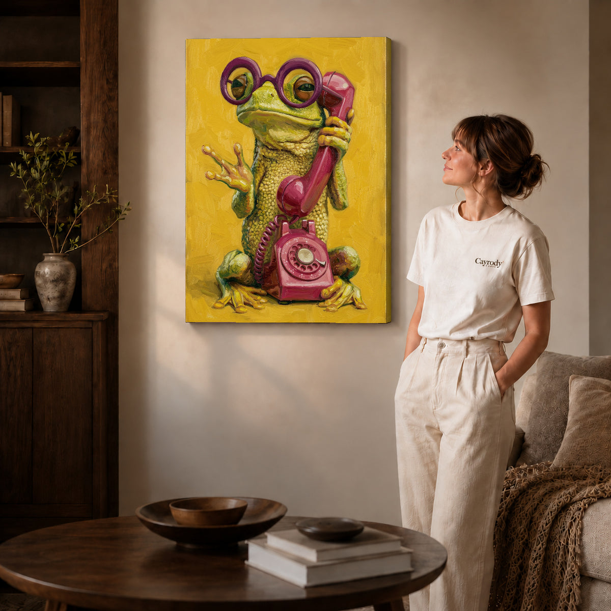Gallery wrapped chatty telephone frog artwork with shaded canvas edges beside a woman wearing cream clothing.