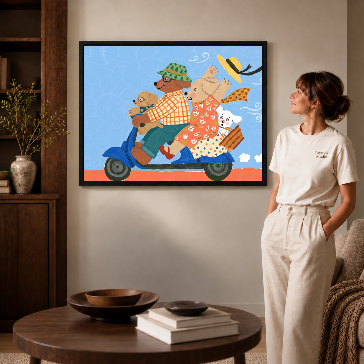Black framed scooter dog family artwork beside a woman in a warm neutral living room.